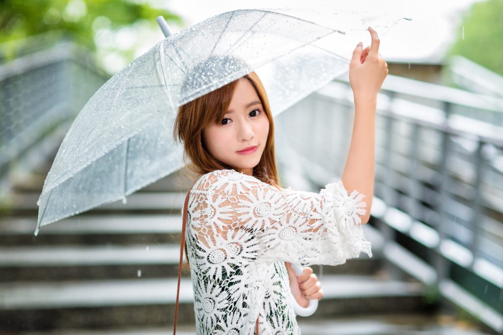 雨で傘をさすまつげエクステする女性の写真
